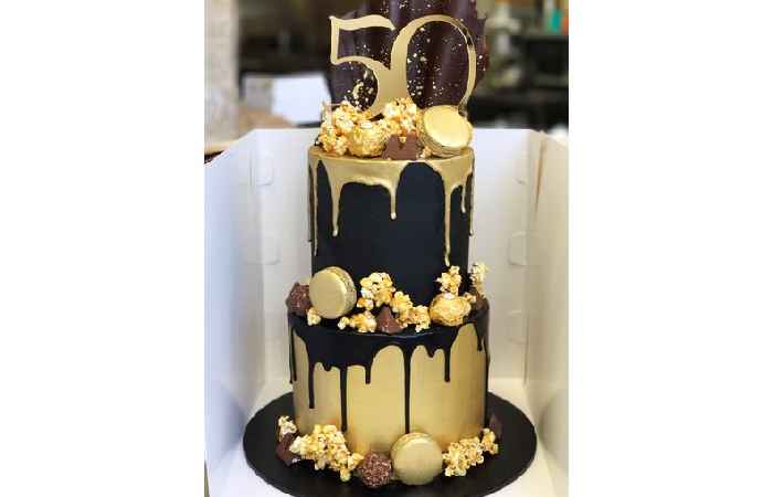 Black and gold two tier with caramel popcorn, macarons, chocolate drip and custom cake topper